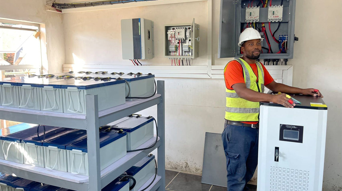 An engineer stands next to a large Anern off-grid solar inverter unit with rows of batteries stored on metal racks